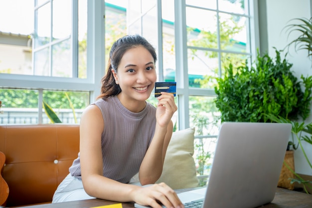 La mujer asiática tiene tarjeta de crédito y usa compras en línea desde el teléfono inteligente en casa.