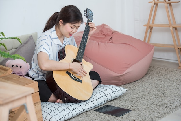 Mujer asiática tocando la guitarra con tableta