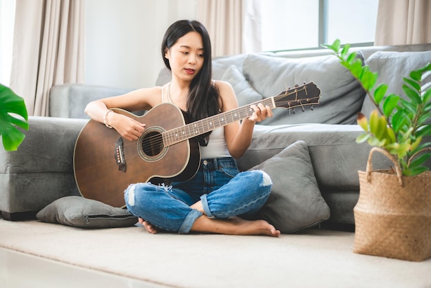 Mujer asiática tocando música con guitarra en casa joven guitarrista músico estilo de vida con instrumento de arte acústico sentado para tocar y cantar una canción haciendo sonido en hobby en la habitación de la casa