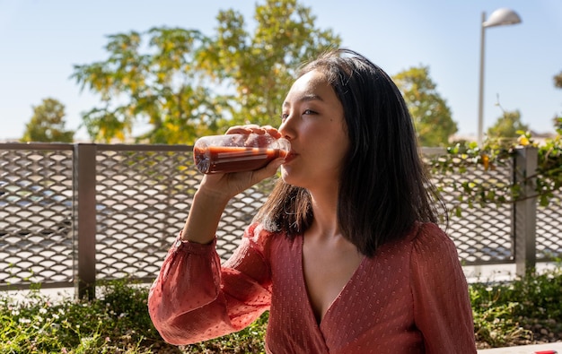 Mujer asiática tomando un batido saludable de una botella de plástico. vista horizontal de la cintura para arriba