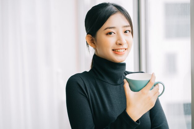 Mujer asiática tomando café junto a la ventana durante el descanso