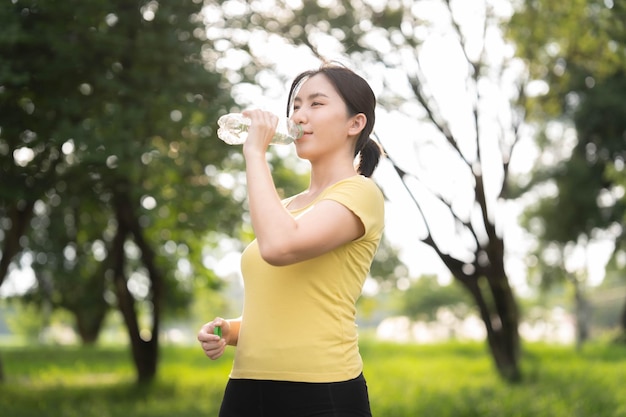 Foto mujer asiática tomando un descanso para beber agua después de trotar en el parque el concepto de beber mucha agua para hacer ejercicio saludable al aire libre