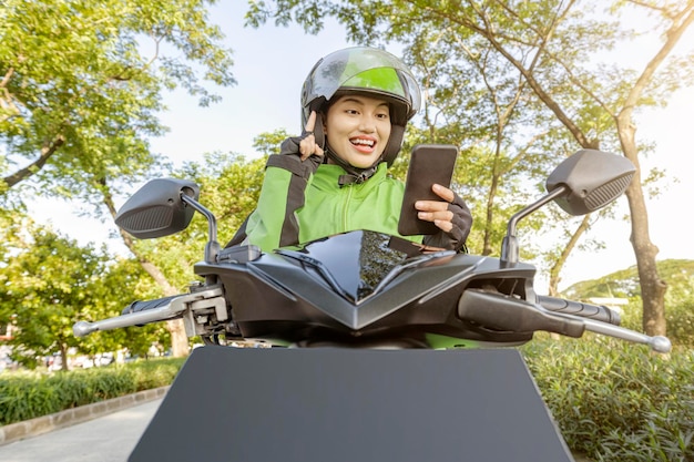 Mujer asiática trabaja como taxista de motocicletas revisando el pedido en su teléfono móvil