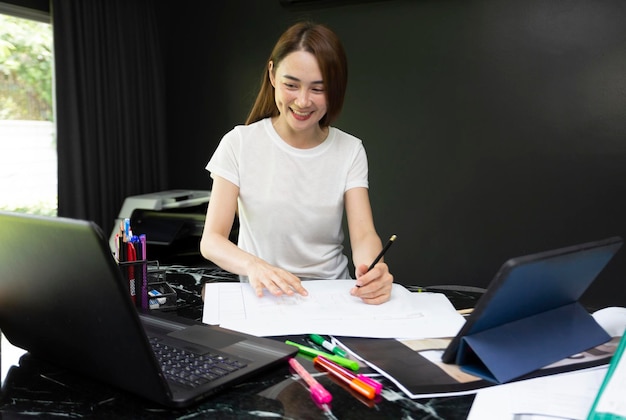 Mujer asiática trabaja en herramientas digitales tableta portátil móvil con dibujo en plan de impresión azul