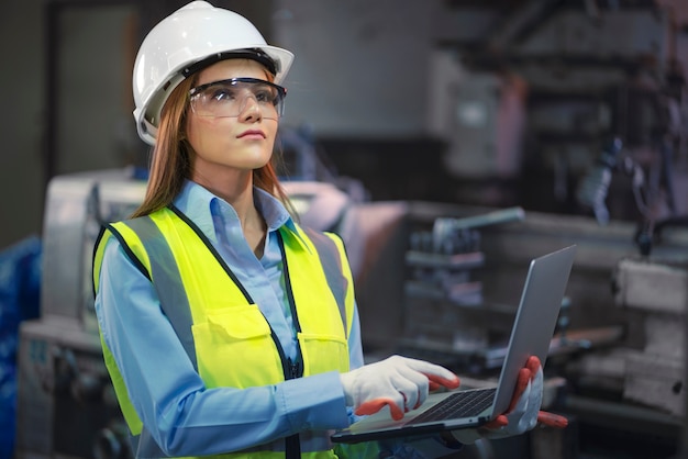 La mujer asiática del trabajador de la fábrica sostiene la computadora portátil y la sonrisa también mira a la cámara en el área de trabajo