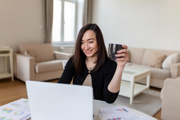 Mujer asiática trabajando en una computadora portátil sonriendo Mujer trabajando desde casa en una computadora portátil en un apartamento moderno Mujer de moda trabajando en una computadora portátil desde casa