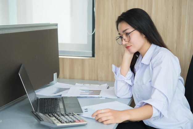 Mujer asiática trabajando horas extras en la oficina Negocios mucho trabajo Revisar archivo con laptop Gente tailandesa con uniforme de oficina