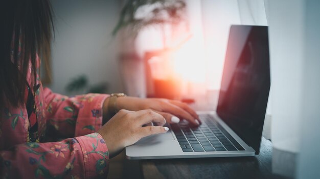 Mujer asiática trabajando en una laptop mientras está sentada en una oficina creativa o en un café. Niña asiática trabajando con una laptop en la mesa de madera del café.