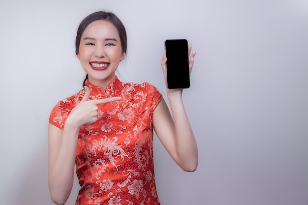 Mujer asiática en traje nacional del año nuevo chino con teléfono inteligente en fondo aislado suave