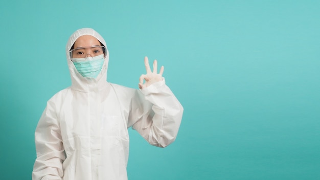 Mujer asiática en traje de ppe use mascarilla y guantes médicos es hacer un signo de mano ok sobre fondo de menta