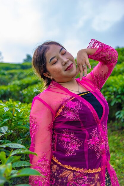 Foto una mujer asiática en un traje rosa tradicional está de pie muy elegantemente en una plantación de té