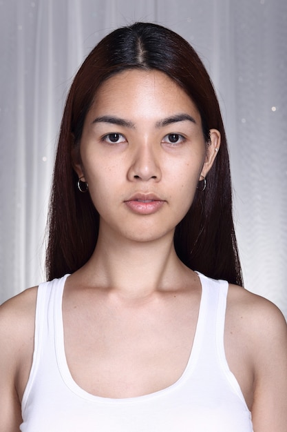 Mujer asiática transgénero antes de maquillaje morena estilo de pelo. sin retoques, rostro fresco con piel agradable y tersa. Iluminación de estudio, fondo gris, retrato