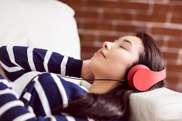 Mujer asiática tumbada en el sofá escuchando música