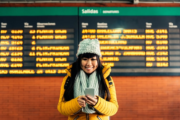 Mujer asiática turística con móvil en la estación de tren. Concepto de turismo.