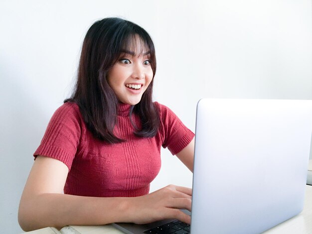Mujer asiática usa camisa roja con laptop sintiéndose emocionada grita de alegría y felicidad sorpresa ganadora expresión fondo blanco mujeres indonesias