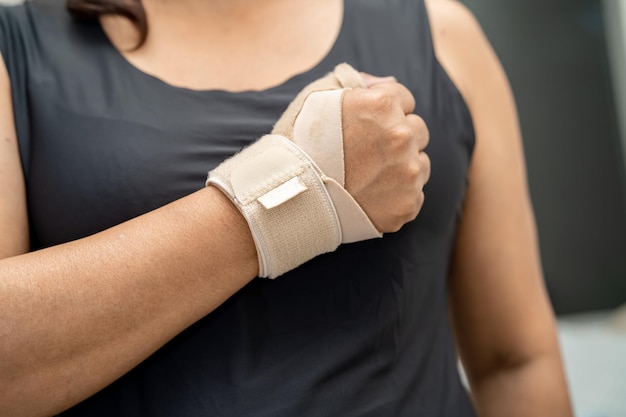 Mujer asiática usa vendaje elástico para tratar el síndrome de De Quervain en la mano y el dedo en la oficina
