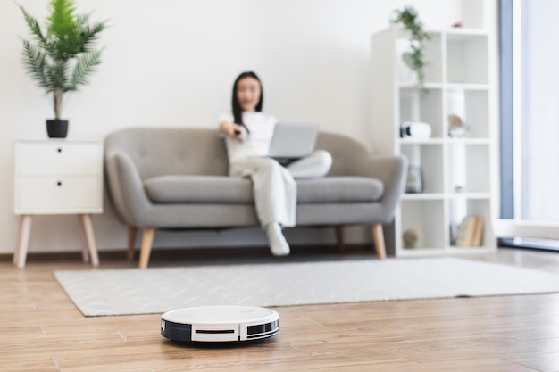 Mujer asiática usando una aspiradora robot para la limpieza moderna del hogar
