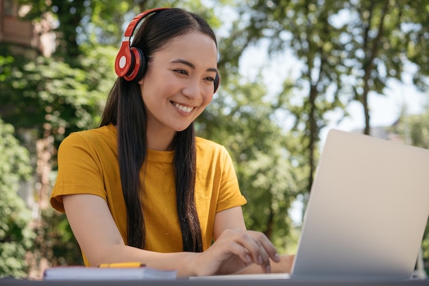 Mujer asiática usando audífonos con comunicación de computadora portátil en línea