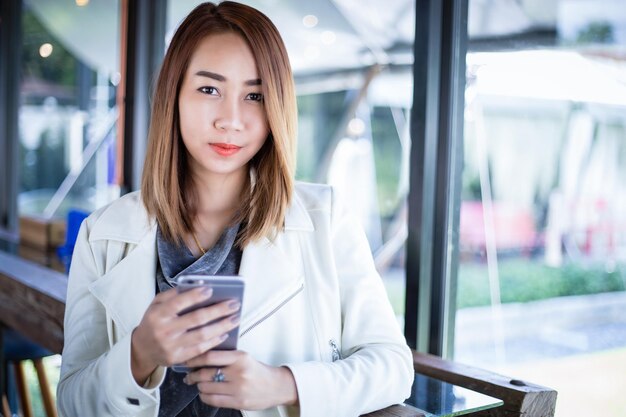 Mujer asiática usando el teléfono para comprar en línea y llamando con el teléfono celular en la cafetería