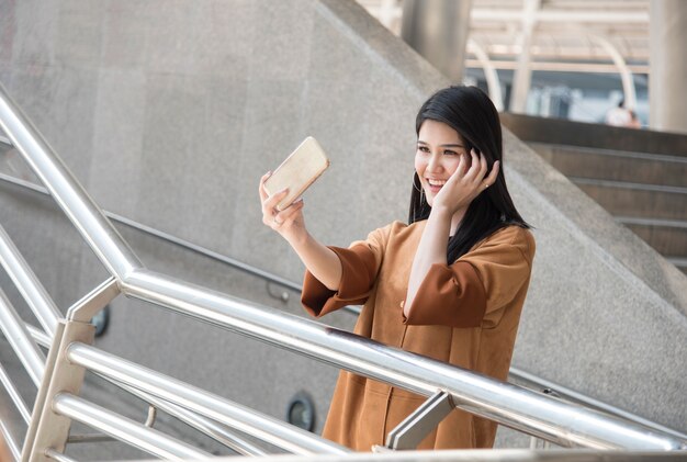 mujer asiática usando teléfono inteligente tomando una foto selfie en la ciudad.