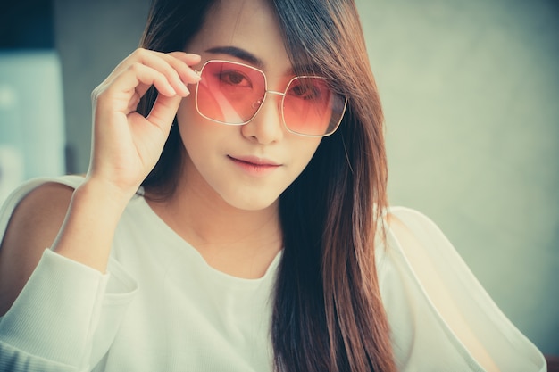 Mujer asiática usar gafas de sol y sentado en una cafetería.