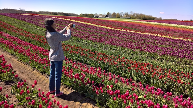 Mujer asiática usar teléfono móvil tomar fotos en el campo de tulipanes