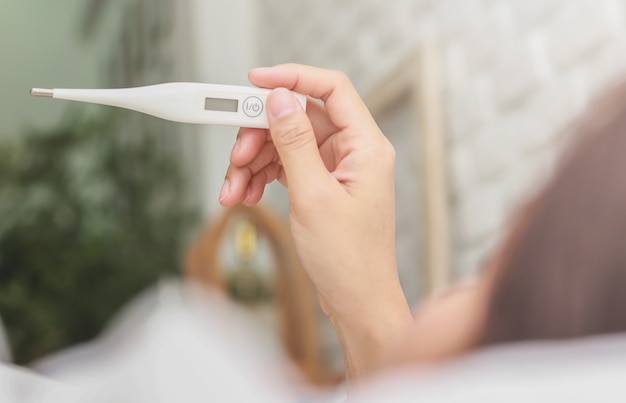 Mujer asiática utiliza un termómetro para detectar la fiebre en el dormitorio.