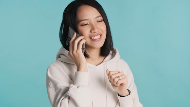 Mujer asiática vestida con capucha hablando por teléfono inteligente aislado sobre fondo colorido Comunicación distante