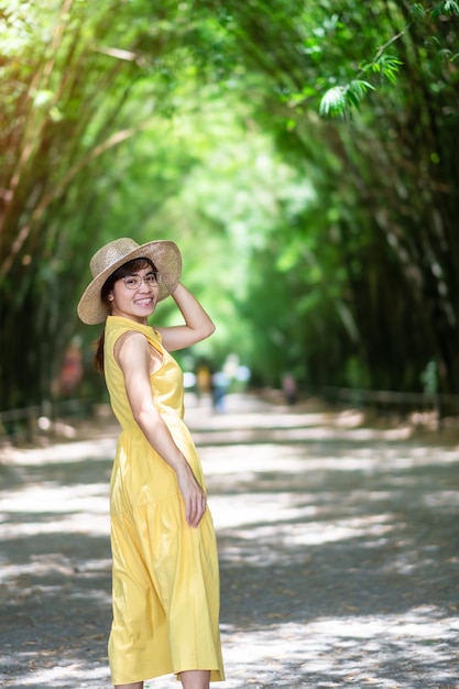 Foto mujer asiática en vestido amarillo y sombrero viajando en el túnel de bambú verde viajero feliz caminando chulabhorn wanaram templo emblemático y popular para las atracciones turísticas en nakhon nayok tailandia