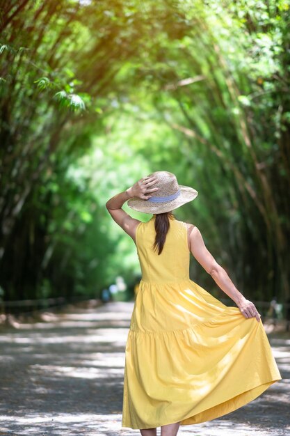 Foto mujer asiática en vestido amarillo y sombrero viajando en el túnel de bambú verde viajero feliz caminando chulabhorn wanaram templo emblemático y popular para las atracciones turísticas en nakhon nayok tailandia