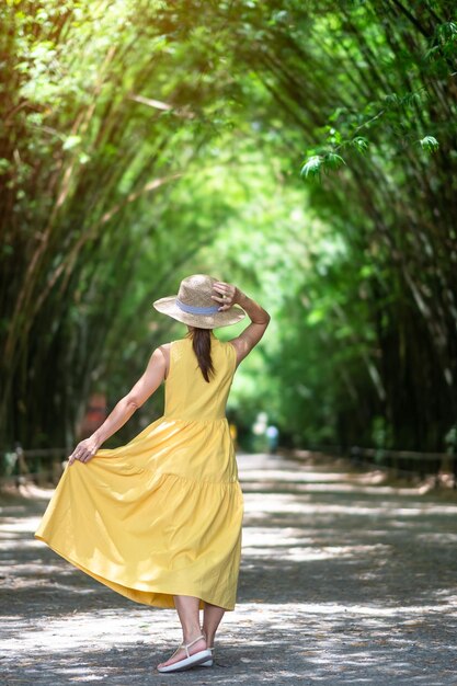 Foto mujer asiática en vestido amarillo y sombrero viajando en el túnel de bambú verde viajero feliz caminando chulabhorn wanaram templo emblemático y popular para las atracciones turísticas en nakhon nayok tailandia