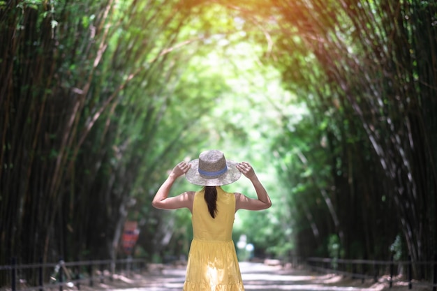 Foto mujer asiática en vestido amarillo y sombrero viajando en el túnel de bambú verde viajero feliz caminando chulabhorn wanaram templo emblemático y popular para las atracciones turísticas en nakhon nayok tailandia