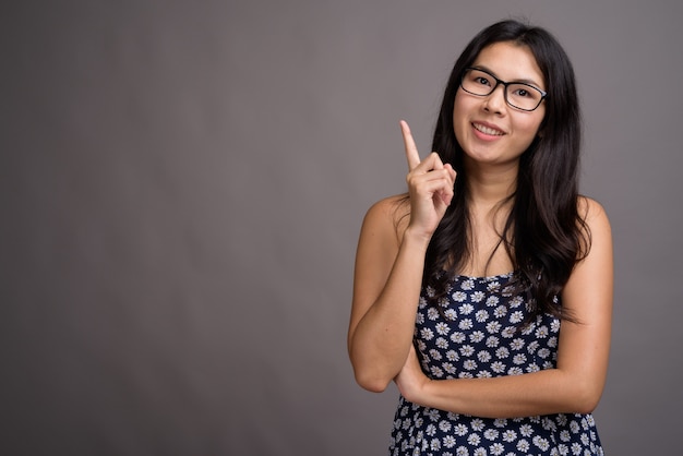 Mujer asiática con vestido azul y anteojos contra el espacio gris