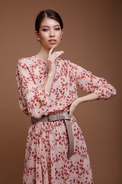 Mujer asiática en vestido beige estampado de flores posando sobre fondo café marrón Retrato de tiro de estudio