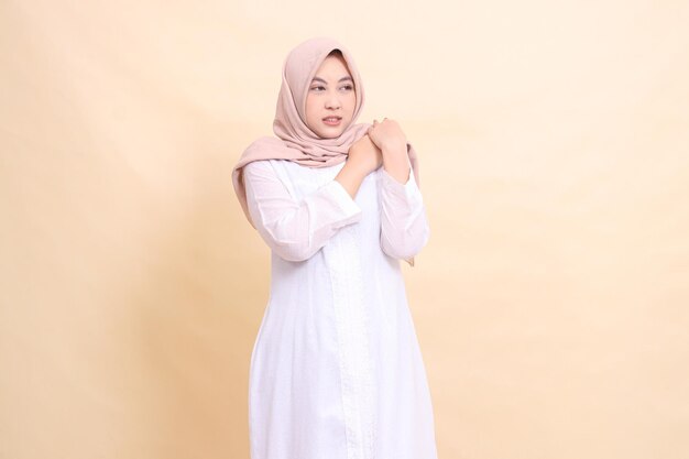 mujer asiática con un vestido blanco sincero hijab está de pie en el dolor con ambas manos sosteniendo su hombro