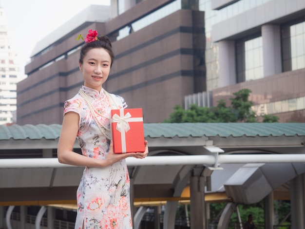 Mujer asiática en vestido chino con caja de regalo roja en la mano con fondo de ciudad