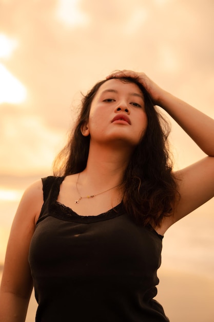 Una mujer asiática con un vestido negro y un cuerpo regordete adopta una pose muy coqueta mientras disfruta de la playa.