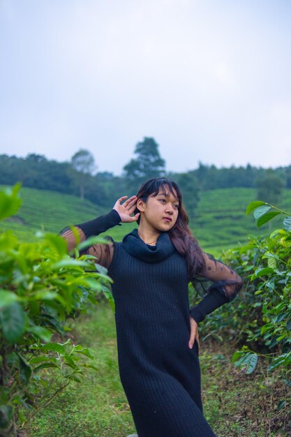 una mujer asiática en un vestido negro está posando frente a una muy hermosa plantación de té por la mañana