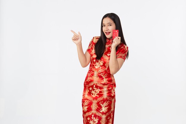 Mujer asiática con vestido qipao oriental mostrando tarjeta de crédito roja en mano en superficie de estudio aislado gris claro