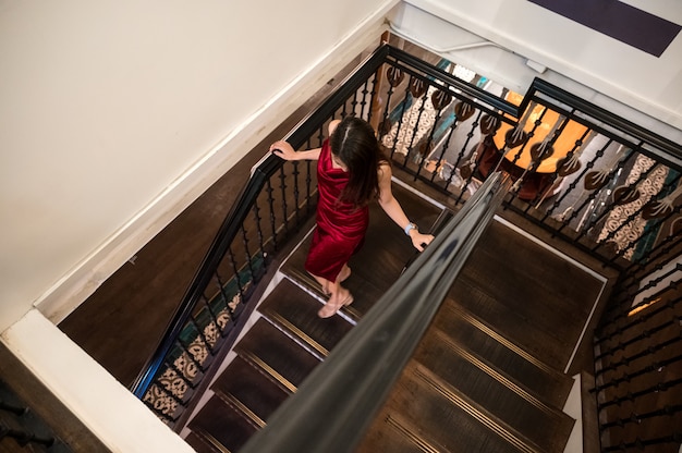 Mujer asiática en vestido rojo bajando de escaleras antiguas en el hotel