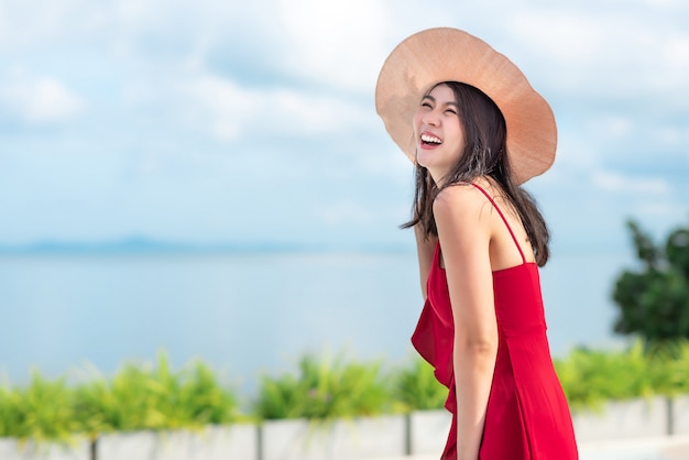 Mujer asiática en vestido rojo disfruta de sus vacaciones en un día soleado