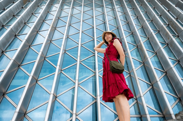 Mujer asiática en vestido rojo en edificio moderno, chica femenina con estilo de vida urbano