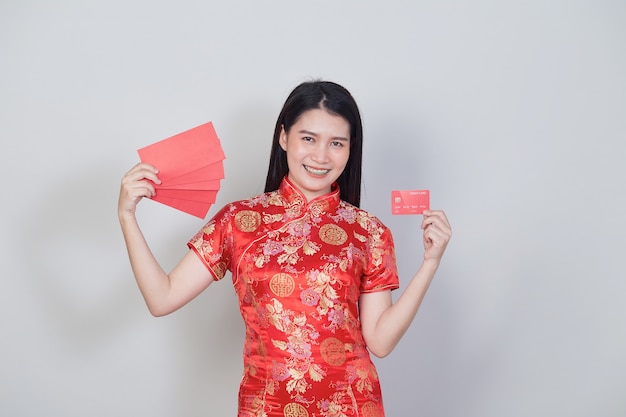 Mujer asiática con vestido tradicional cheongsam qipao mostrando tarjetas de crédito y sobres rojos para conceptos de compras del año nuevo chino.