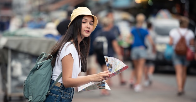 Foto mujer asiática del viajero en mercado callejero con el mapa, en la ciudad de bangkok de tailandia.