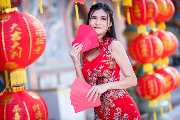 Mujer asiática vistiendo rojo cheongsam chino tradicional, sosteniendo sobres rojos en la mano