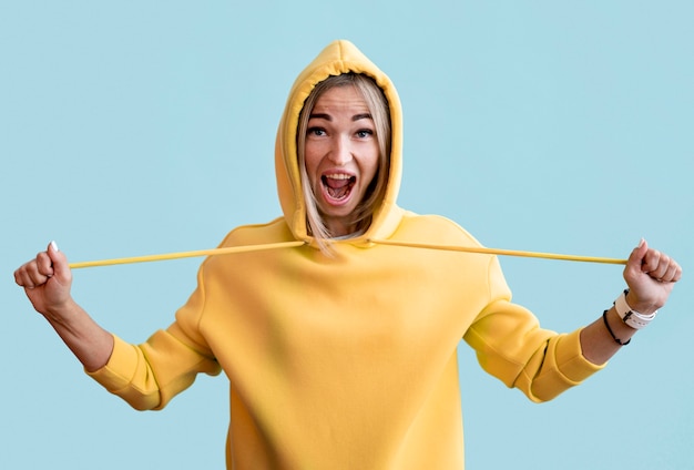 Foto mujer asiática vistiendo una sudadera con capucha amarilla sobre fondo azul.