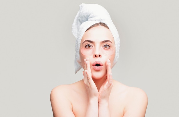Mujer asombrada aplicando parches en los ojos Retrato de mujer con toalla en la cabeza Retrato de mujer de belleza con parches en los ojos que muestran un efecto de piel perfecta Máscara de ojos parches cosméticos rostro de mujer en primer plano