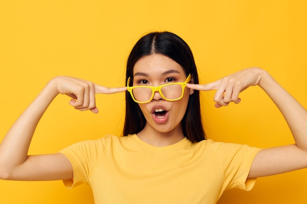 Mujer con aspecto asiático en camisetas amarillas con anteojos posando moda fondo amarillo inalterado