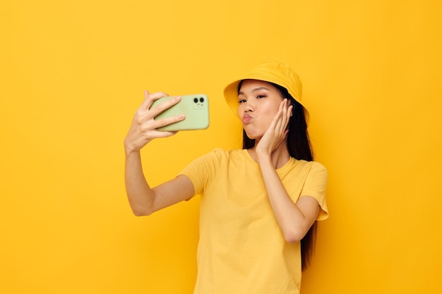 Mujer con aspecto asiático hablando por teléfono posando moda fondo amarillo inalterado