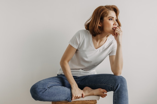 Mujer de aspecto fresco en camiseta blanca y jean relajarse en la habitación de su apartamento